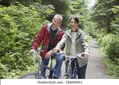 Portrait Of Happy Mature Man And Middle Aged Woman With Bikes On Forest Road