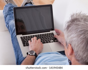 Portrait Of Happy Mature Man Using Laptop On Couch