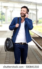 Portrait Of Happy Mature Man Walking On Train Station And Using Mobile Phone