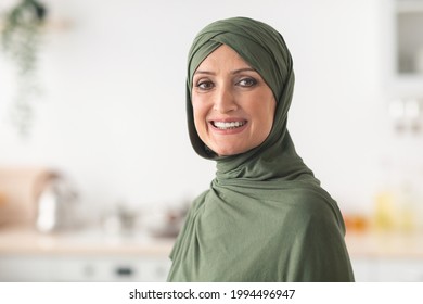 Portrait Of Happy Mature Muslim Lady Wearing Hijab Standing In Kitchen At Home. Modern Middle-Eastern Housewife Posing Indoors, Smiling To Camera. Headshot Of Beautiful Arab Female