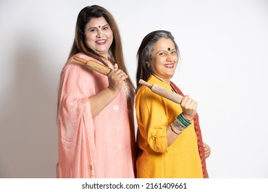 Portrait Of Happy Mature Senior And Young Indian Woman Holding Rolling Pin And Wooden Spoon Isolated On White Background. Home Maker, Kitchen Concept.