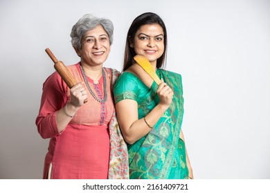 Portrait Of Happy Mature Senior And Young Indian Woman Holding Rolling Pin And Wooden Spoon Isolated On White Background. Home Maker, Kitchen Concept.