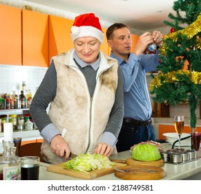 Portrait Of Happy Mature Woman Cooking Salad For Celebration Of Christmas At Home, Adult Man On Background