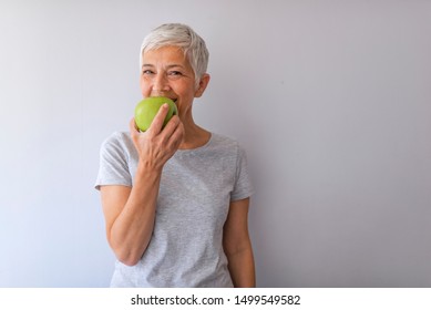 Portrait of happy mature woman holding granny smith apple at home. Beautiful senior woman over grunge grey wall eating green apple with happy face smiling.  - Powered by Shutterstock