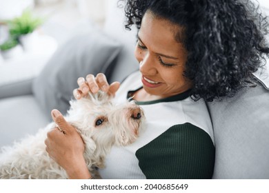 Portrait Of Happy Mature Woman Sitting Indoors At Home, Playing With Dog.