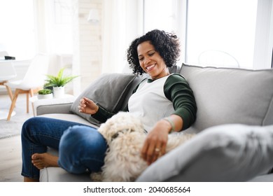 Portrait Of Happy Mature Woman Sitting Indoors At Home, Playing With Dog.