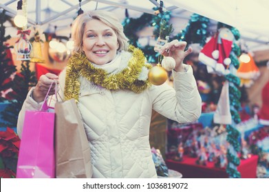 Portrait Of Happy Mature Woman In Tinsel With Christmas Toys At Fair Outdoor
