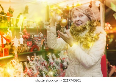 Portrait Of Happy Mature Woman In Tinsel With Christmas Toys At Fair Outdoor.