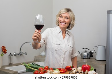 Portrait Of A Happy Mature Woman With Vegetables And Wine Glass In The Kitchen At Home