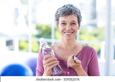 Portrait Of Happy Mature Woman With Water Bottle In Fitness Studio