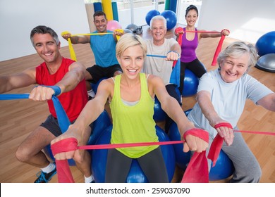 Portrait of happy men and women on fitness balls exercising with resistance bands in gym class - Powered by Shutterstock