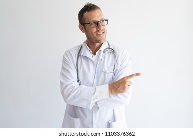 Portrait Of Happy Mid Adult Doctor In Glasses Pointing Direction. Caucasian General Practitioner Wearing Lab Coat And Stethoscope Pointing At Something With Forefinger. Advertising Concept