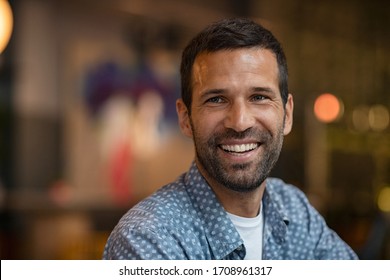 Portrait of happy mid adult man with beard. Close up of successful young entrepreneur in casual smiling and looking away. Hopeful business man smiling sitting in cafe; future and vision concept.