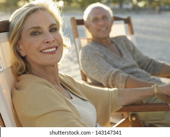 Portrait of happy middle age woman with man relaxing on deckchairs at beach