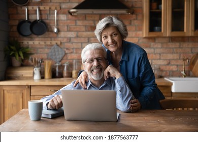 Portrait of happy middle aged family couple enjoying using computer applications or web surfing at home. Smiling bonding old generation man and woman looking at camera, sitting at table with laptop.