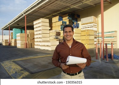 Portrait of happy middle aged man with clipboard standing in front of timber factory - Powered by Shutterstock