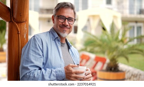 Portrait of happy middle aged man at home outdoor on terrace in garden, relaxing, drinking morning coffee, smiling. - Powered by Shutterstock