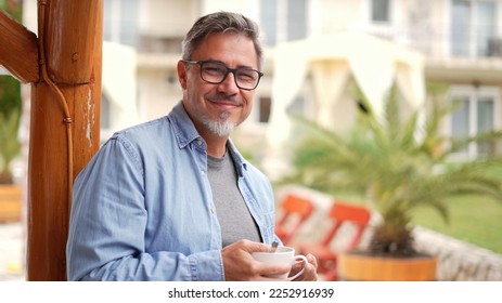 Portrait of happy middle aged man at home outdoor on terrace in garden, relaxing, drinking morning coffee, smiling. - Powered by Shutterstock