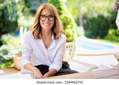 Portrait Of Happy Middle Aged Woman Sitting In A Lounge Chair While Relaxing At The Backyard.