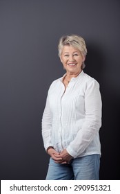 Portrait Of A Happy Middle Aged Woman In Casual Shirt And Jeans, Leaning Against Gray Wall Background And Smiling At The Camera.