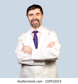 Portrait of happy middle-aged dentist on a pale background, wearing lab coat, dentist mirror in his hand