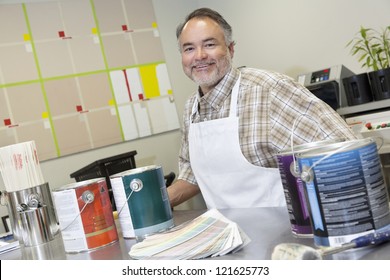 Portrait Of A Happy Middle-aged Sales Clerk At Counter With Paint Cans In Hardware Store