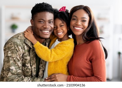 Portrait Of Happy Military Family, Black Soldier Father, Wife And Little Daughter Embracing Together At Home, Cheerful African American Man In Camouflage Uniform Hugging With Spouse And Female Child