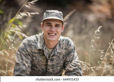 Portrait Of Happy Military Soldier Crouching In Grass In Boot Camp