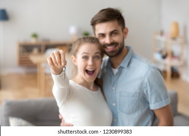 Portrait Of Happy Millennial Couple Hug Holding Key To Own Apartment, Young Husband And Wife Excited To Buy First Home Together, Smiling Married Man And Woman Move In Shared House. Ownership Concept