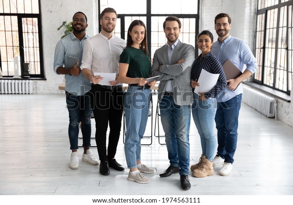 Portrait of happy millennial diverse professional\
team in loft office space. Group of multi ethnic employees\
gathering for corporate meeting and teamwork, looking at camera,\
smiling. Full length
