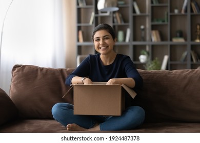 Portrait of happy millennial Indian woman have fun unpack parcel box with order buy online from home. Smiling overjoyed young ethnic female buyer excited shopping on web. Shipping, delivery concept.