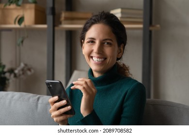 Portrait of happy millennial Latino woman relax on couch at home use modern cellphone gadget texting messaging online. Smiling young Hispanic female client or user browse web on smartphone device.