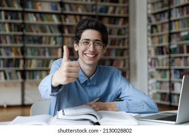 Portrait Of Happy Millennial Smart Male Jewish Student In Eyeglasses Sitting At Table With Laptop And Textbooks, Showing Thumbs Up Gesture, Recommending Educational Online Courses, Studying In Library