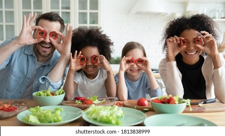 Portrait of happy mixed race diverse couple making grimaces with vegetables, having fun with biracial cute children daughters in kitchen, joyful international family entertaining while cooking food. - Powered by Shutterstock