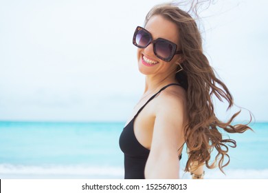 Portrait Of Happy Modern 40 Year Old Woman With Long Curly Hair In Elegant Black Bathing Suit On A White Beach Having Fun Time.