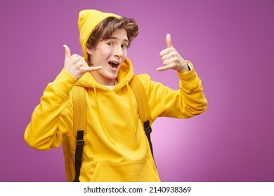 Portrait Of A Happy Modern Teenage Boy In Bright Youth Clothes With Backpack Smiling And Showing Cool Gestures. Purple Background. Youth Fashion And Lifestyle. Bright Youth Colours. Education. 