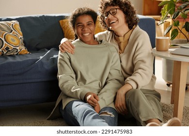 Portrait of happy mom spending time with her adopted daughter, they sitting on the floor in the living room and laughing