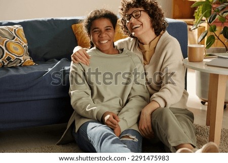 Portrait of happy mom spending time with her adopted daughter, they sitting on the floor in the living room and laughing