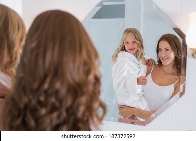 Portrait of a happy mother and daughter looking at bathroom mirror in the house - Powered by Shutterstock