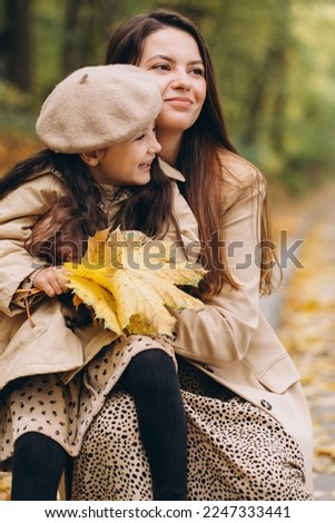 Portrait of happy mother and daughter spending time together in autumn park with falling yellow leaves