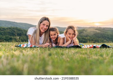 Portrait Of Happy Mother And Daughters Smiling And Laughing Lying On Blanket In Park, They Posing For Photo.