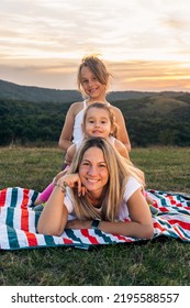 Portrait Of Happy Mother And Daughters Smiling And Laughing Lying On Blanket In Park, They Posing For Photo.