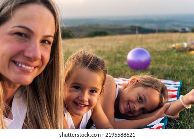 Portrait Of Happy Mother And Daughters Smiling And Laughing Lying On Blanket In Park, They Posing For Photo.