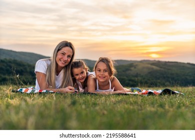 Portrait Of Happy Mother And Daughters Smiling And Laughing Lying On Blanket In Park, They Posing For Photo.