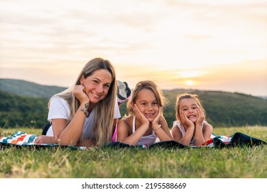 Portrait Of Happy Mother And Daughters Smiling And Laughing Lying On Blanket In Park, They Posing For Photo.