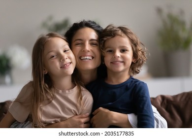 Portrait Of Happy Mother Hugging Two Cute Little Kids. Joyful Affectionate Mom Cuddling Sweet Sibling Son And Daughter, Looking At Camera With Toothy Smile. Family Relationship, Motherhood. Head Shot