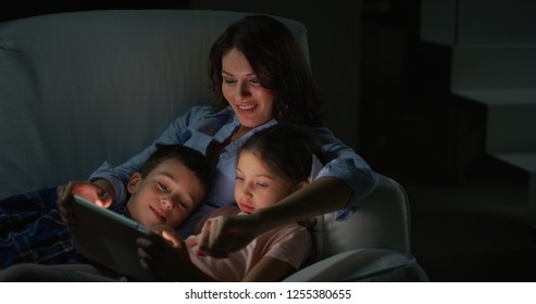 Portrait Of Happy Mother And Kids Using A Tablet On Sofa In The Evening In Slow Motion. Concept Of Family Entertainment, Education, Technology