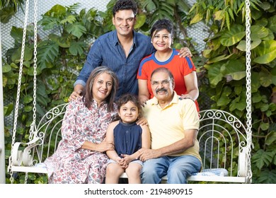 Portrait Of Happy Multi Generational Indian Family Sitting Together On Hanging Swing.