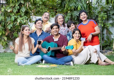 Portrait of happy multi generational indian family sitting enjoy picnic together outdoor garden playing guitar and music having fun. Summer activities  - Powered by Shutterstock