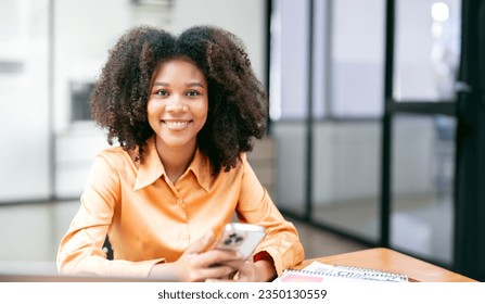 Portrait of happy multiethnic businesswoman using mobile phone. Mixed race young woman looking at camera in creative office. - Shutterstock ID 2350130559